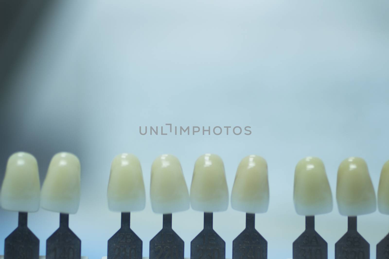 Dentist's tooth color guide used to choose the appropriate natural colors for a patient's tooth implants and crowns on plain blue background of the dental surgery clinic table. Close-up macro photo. 