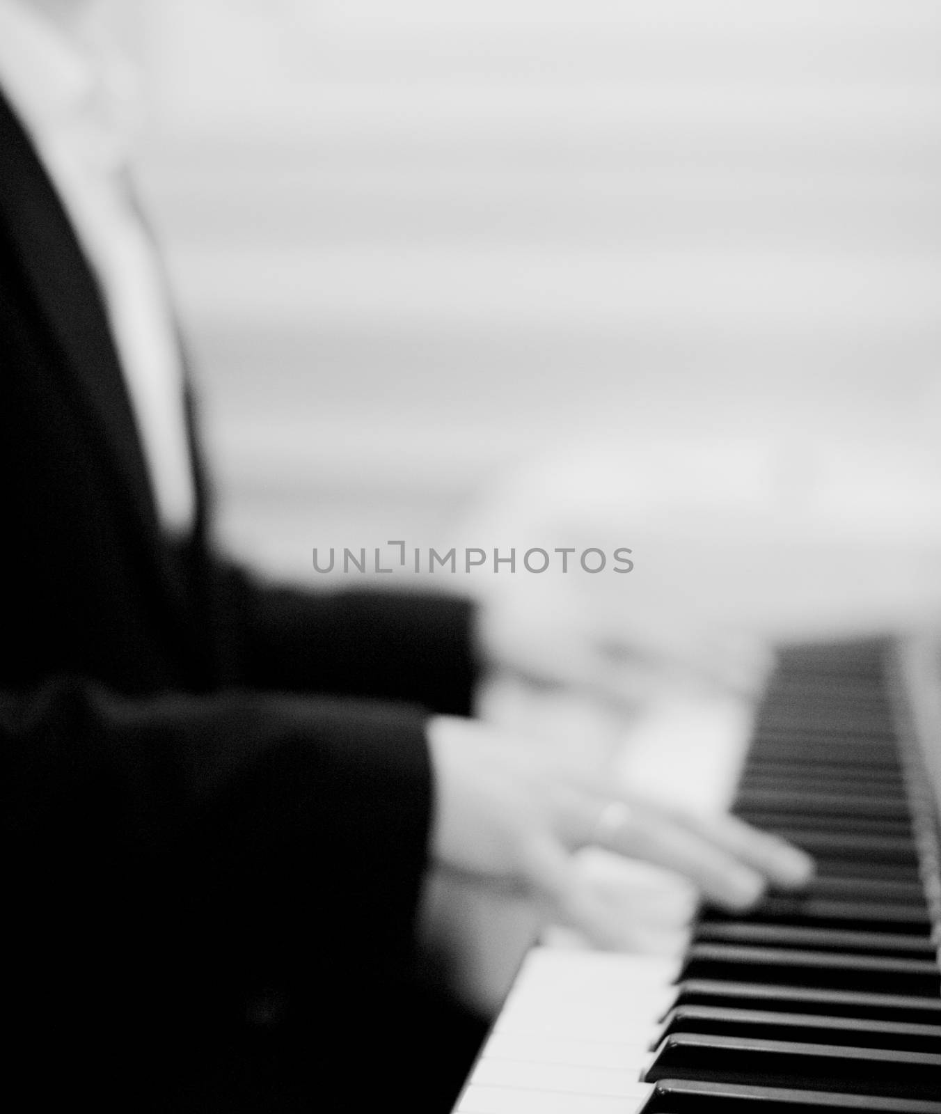 Black and white artistic digital rectangular vertical photo of hand of male pianist playing piano in wedding marriage party in Madrid Spain. Close-up on keys of piano with shallow depth of with background out of focus. 