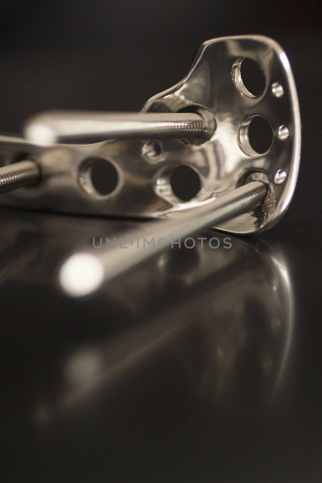 Traumatology orthopedic surgery implant titanium plate and silver color screws in semi silhouette against plain black studio background. Close-up macro photograph in grey tones with reflection and copy space. 