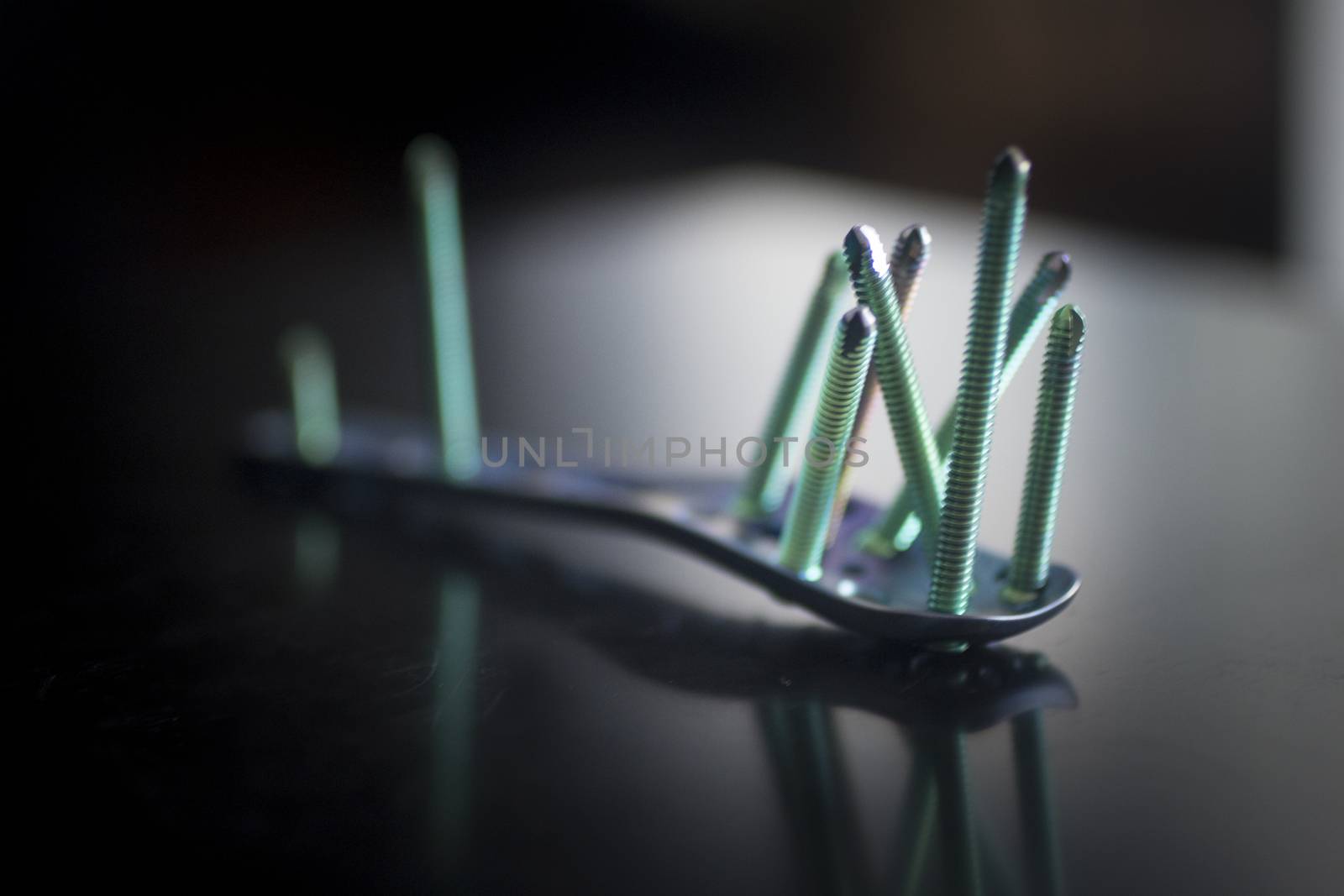 Traumatology orthopedic surgery implant titanium plate and green screws in semi silhouette against plain studio background. Close-up macro photograph in grey tones. 