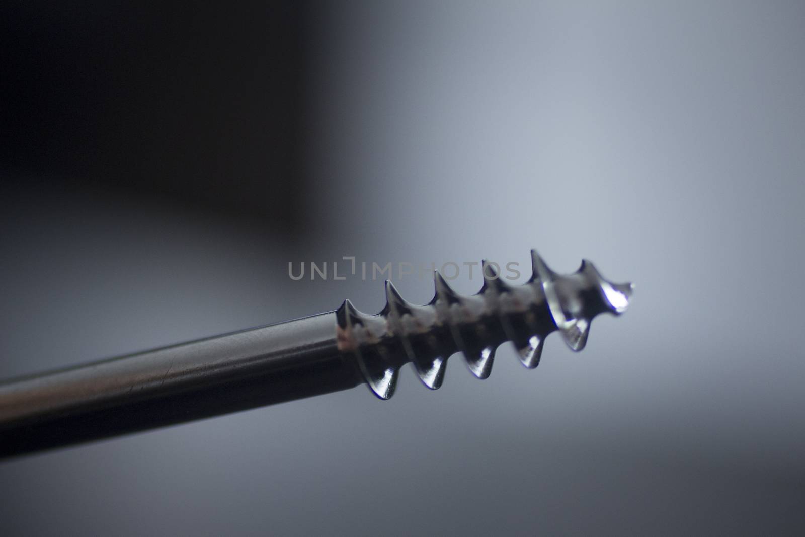 Traumatology orthopedic surgery implant titanium silver gray metal color screw in semi silhouette against plain black studio background. Close-up macro horizontal photograph. 