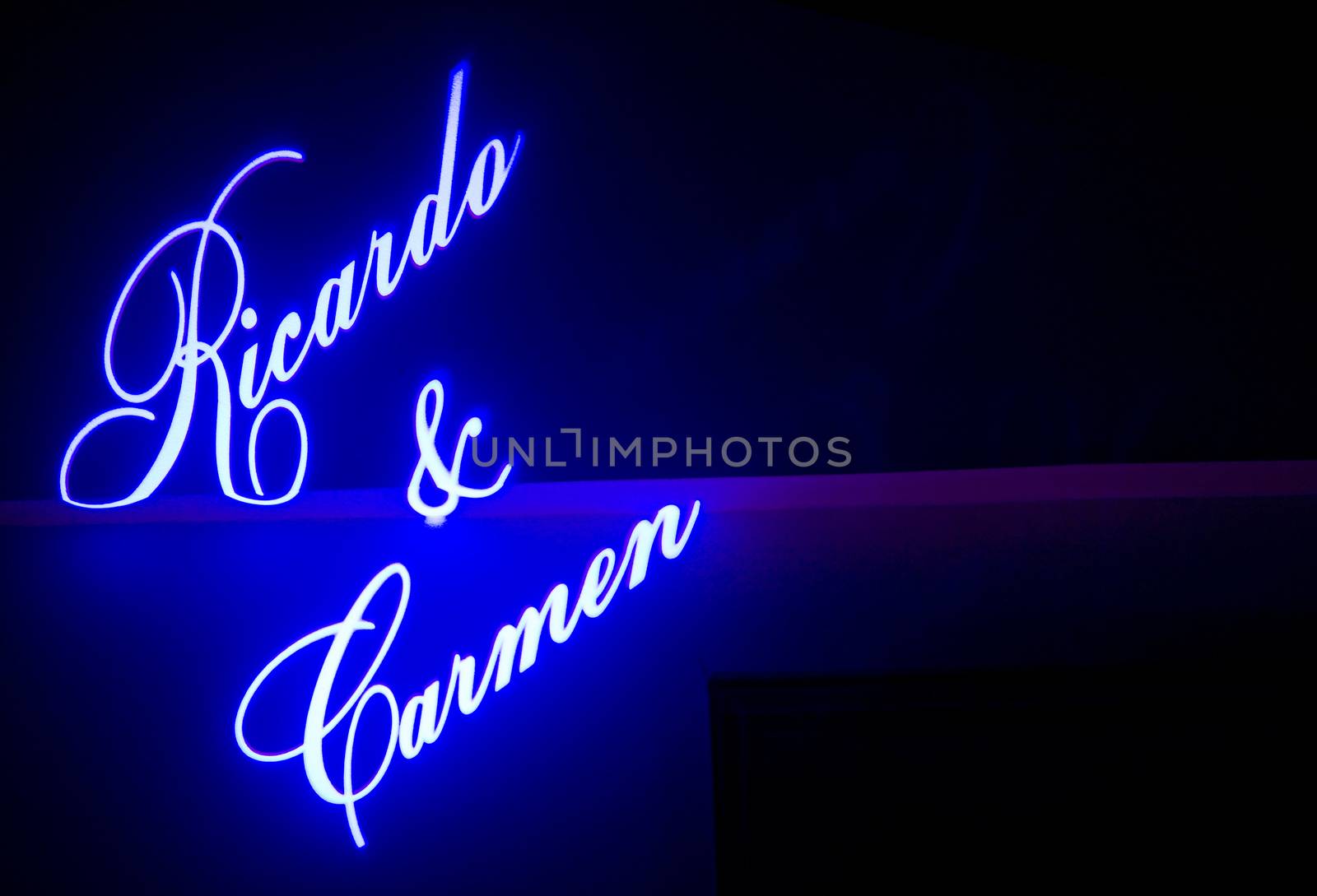 Names of the Spanish wedding bride and groom projected on wall of marriage reception building at night "Carmen & Ricardo". 