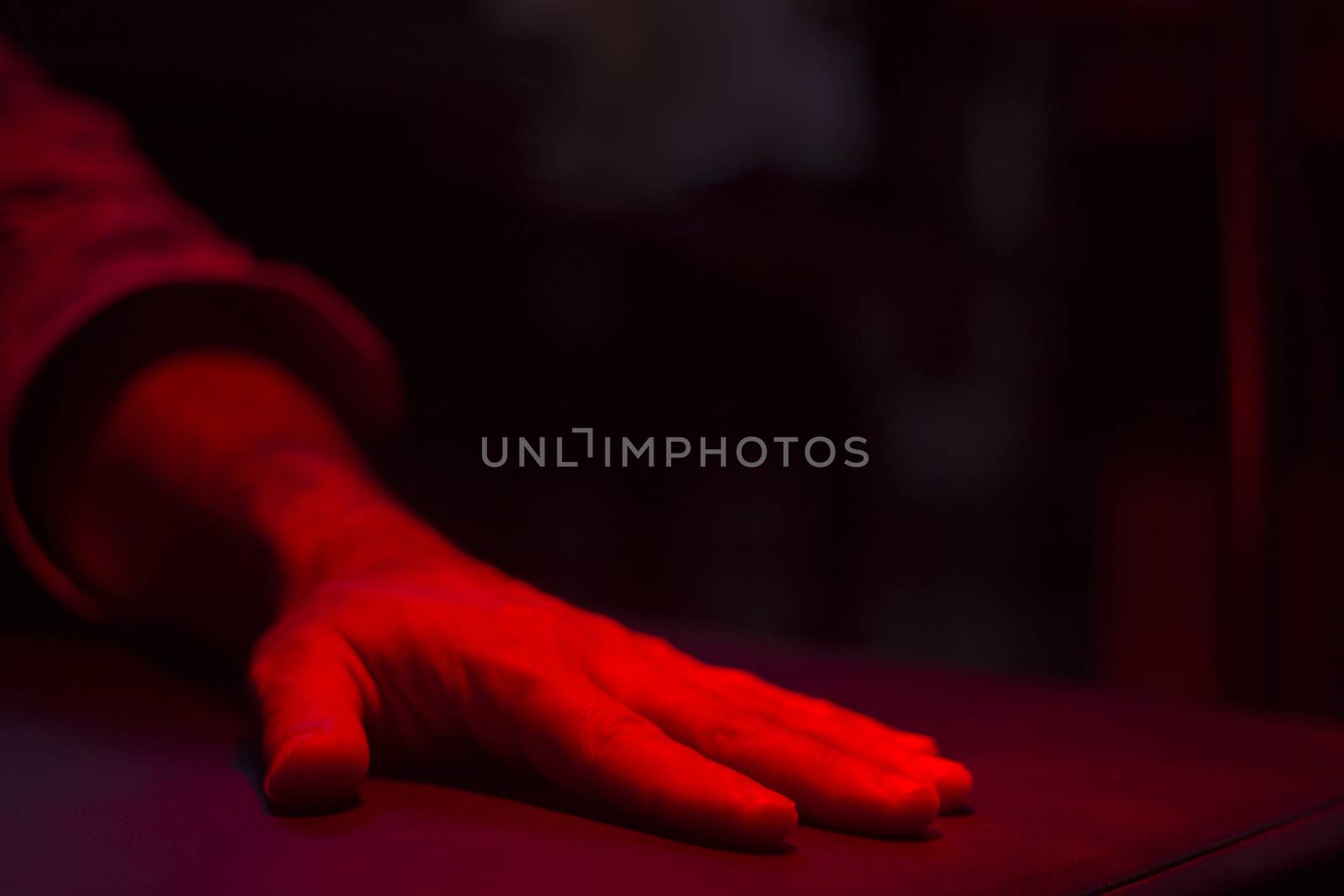 Hand of injured patient receiving treamente under red rehabilitation hospital clinic heat lamp. 