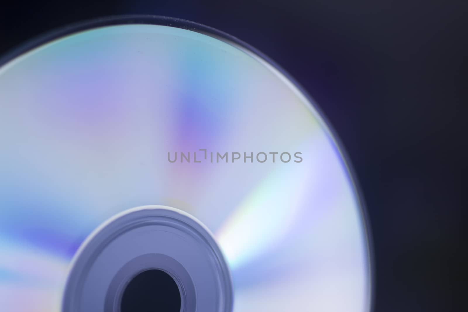 Close-up semi-abstract macro photo of shiny underside of cd dvd cd-rom disk reflecting multicolors in blue purple tone set against black studio background. Artistic color digital photo with shallow depth of focus.