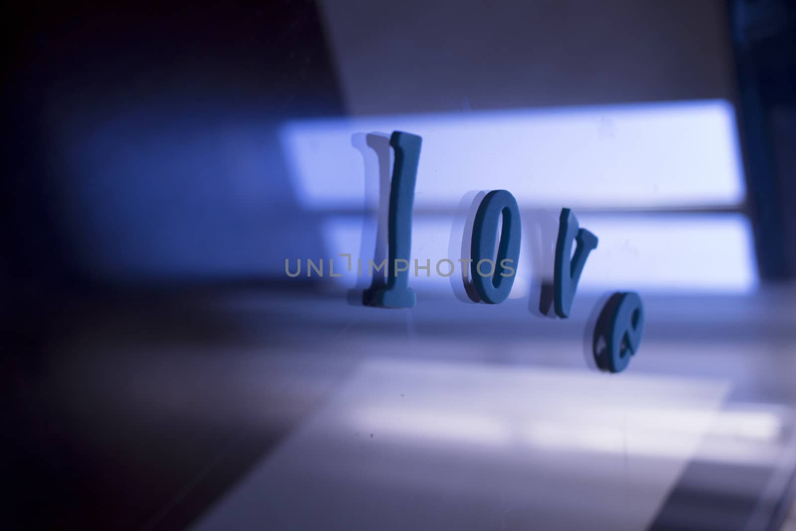 The word love spelled in letters on background of glass coffee table with abstract blue purple defocused artistic effect reflections of evening light. 