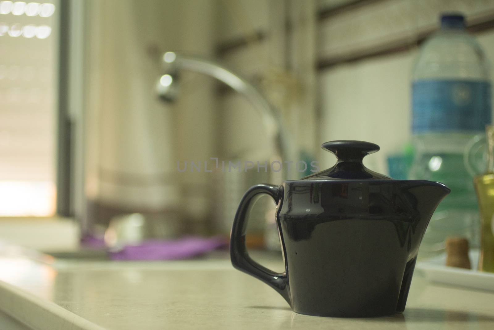 Teapot on domestic home kitchen bench with sink and water bottle in background defocused. 