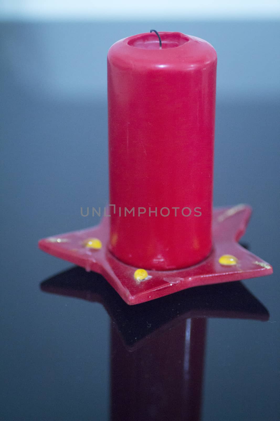One large red Candle on red decorative Christmas star dish on plain studio blue background. 