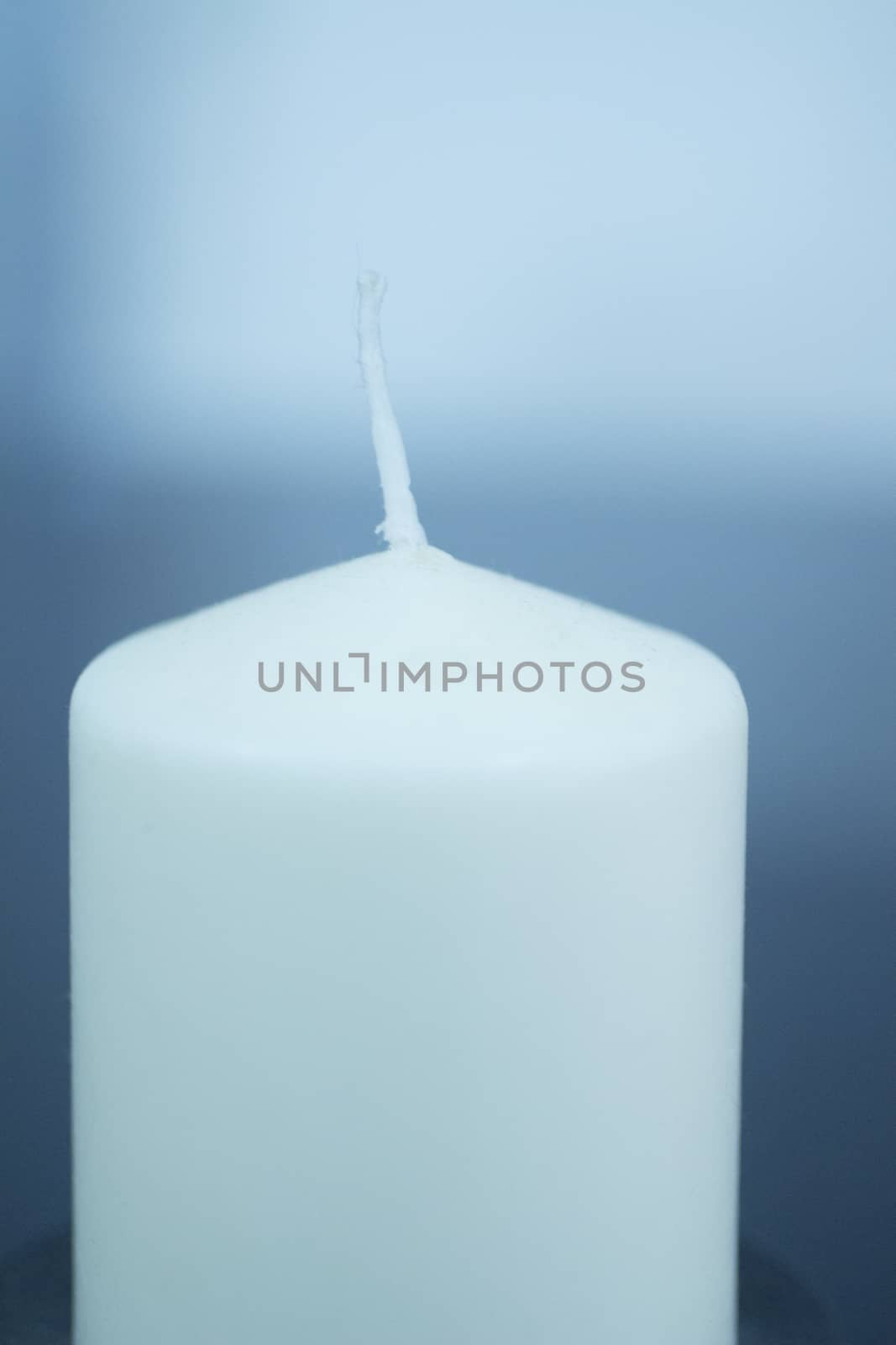 White Candle on plain blue studio background with shallow depth of focus. 