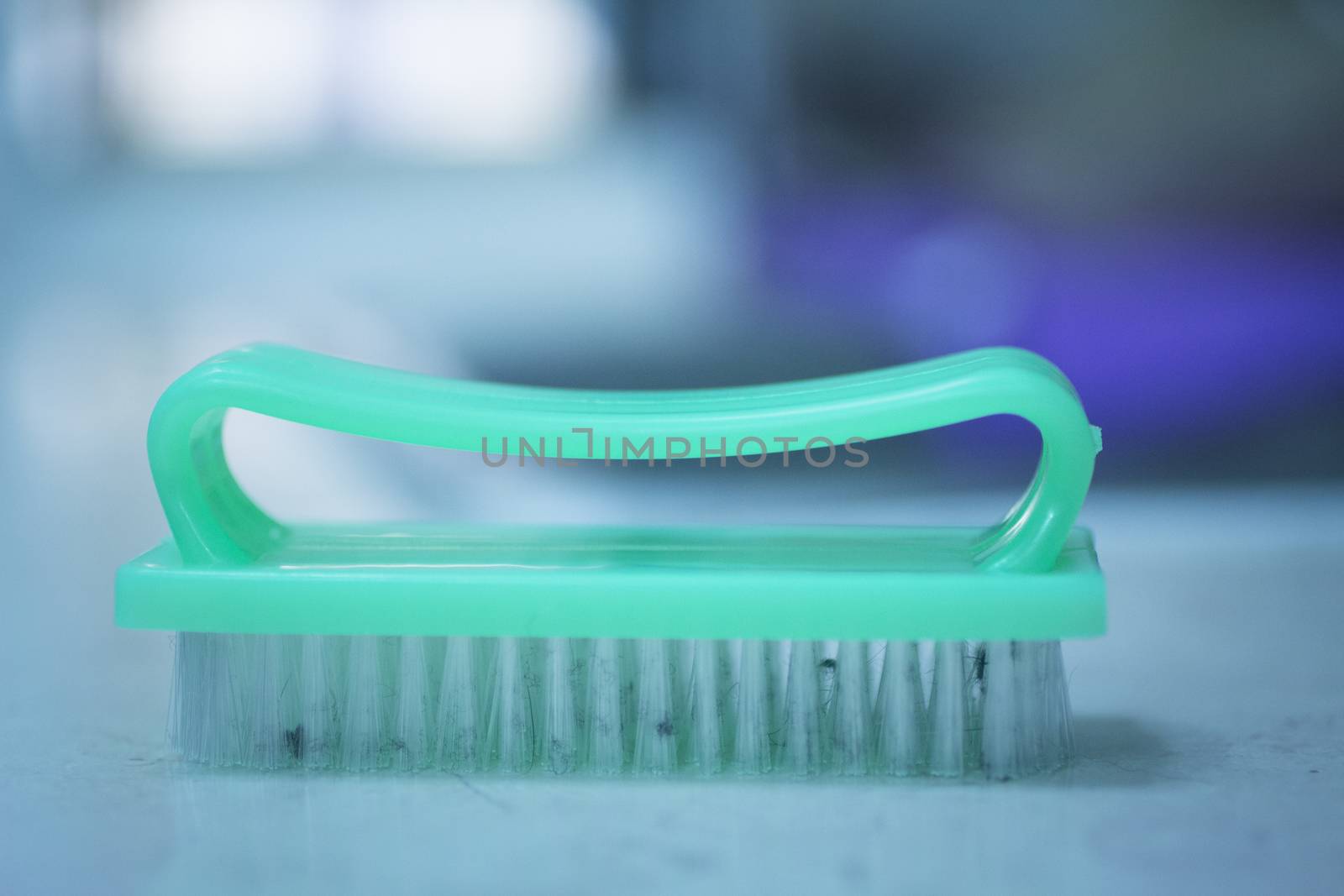 Green plastic scrubbing brush for washing up dirty dishes and plates or for cleaning the bathroom or human nails on kitchen bench with defocused background. 