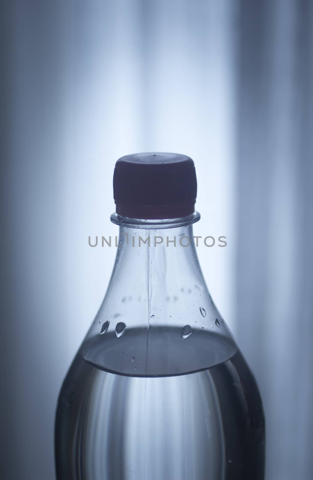 Isolated blue plastic soda lemonade soft drink bottle on a plain blue studio background close-up photo.