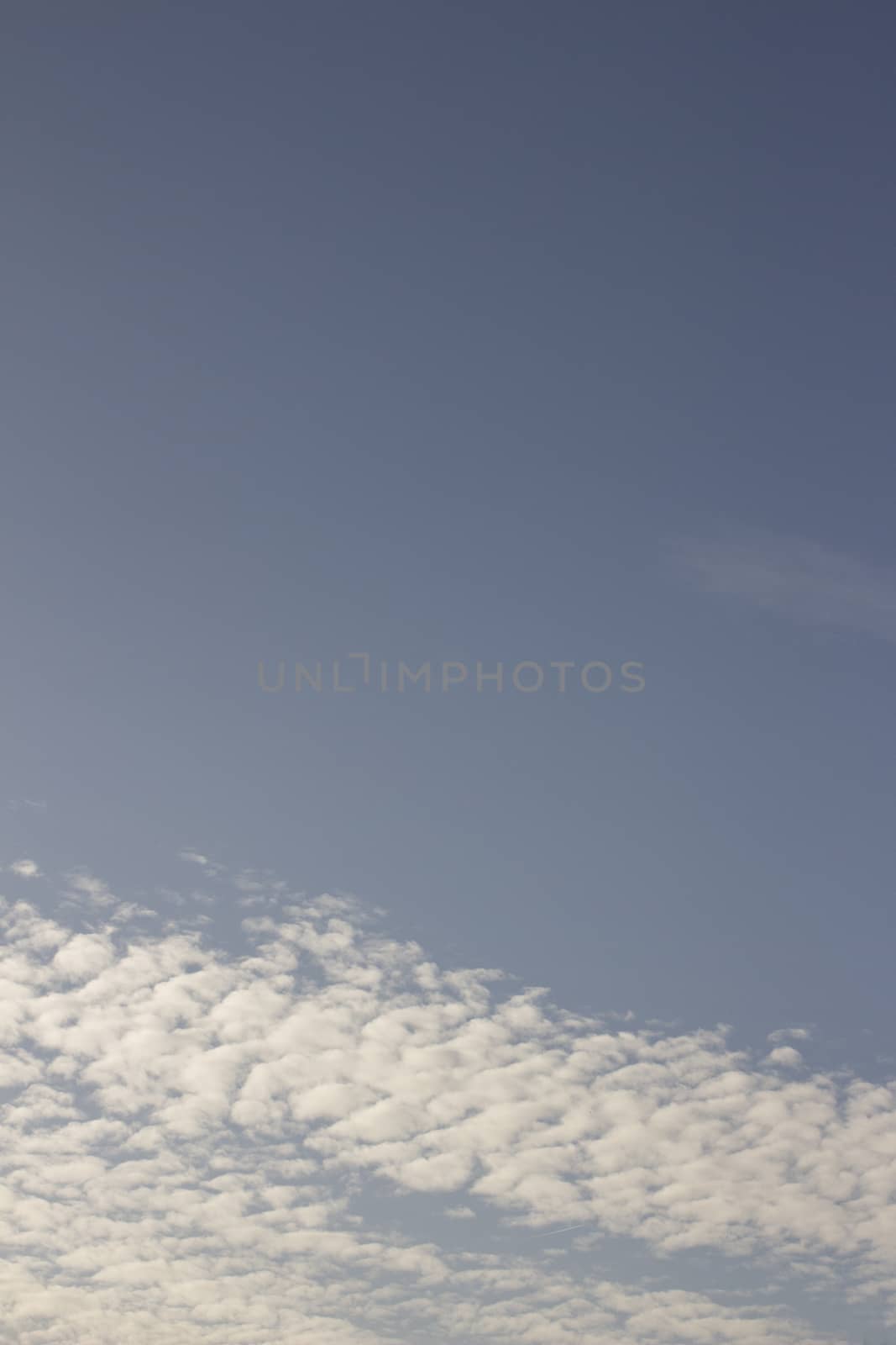 Blue summer sky with soft light white clouds on sunny warm day vertical rectangular photo.