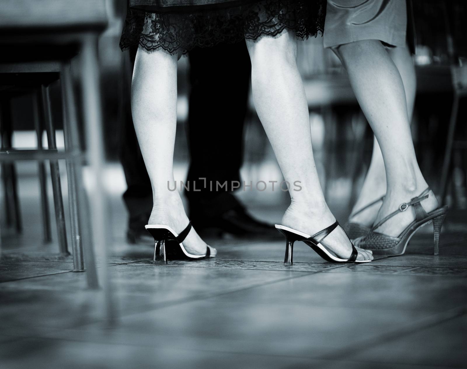 Feet and legs of young women wedding guest in high heel shoes and cocktail party dress in wedding reception blue black and white toned photo. 