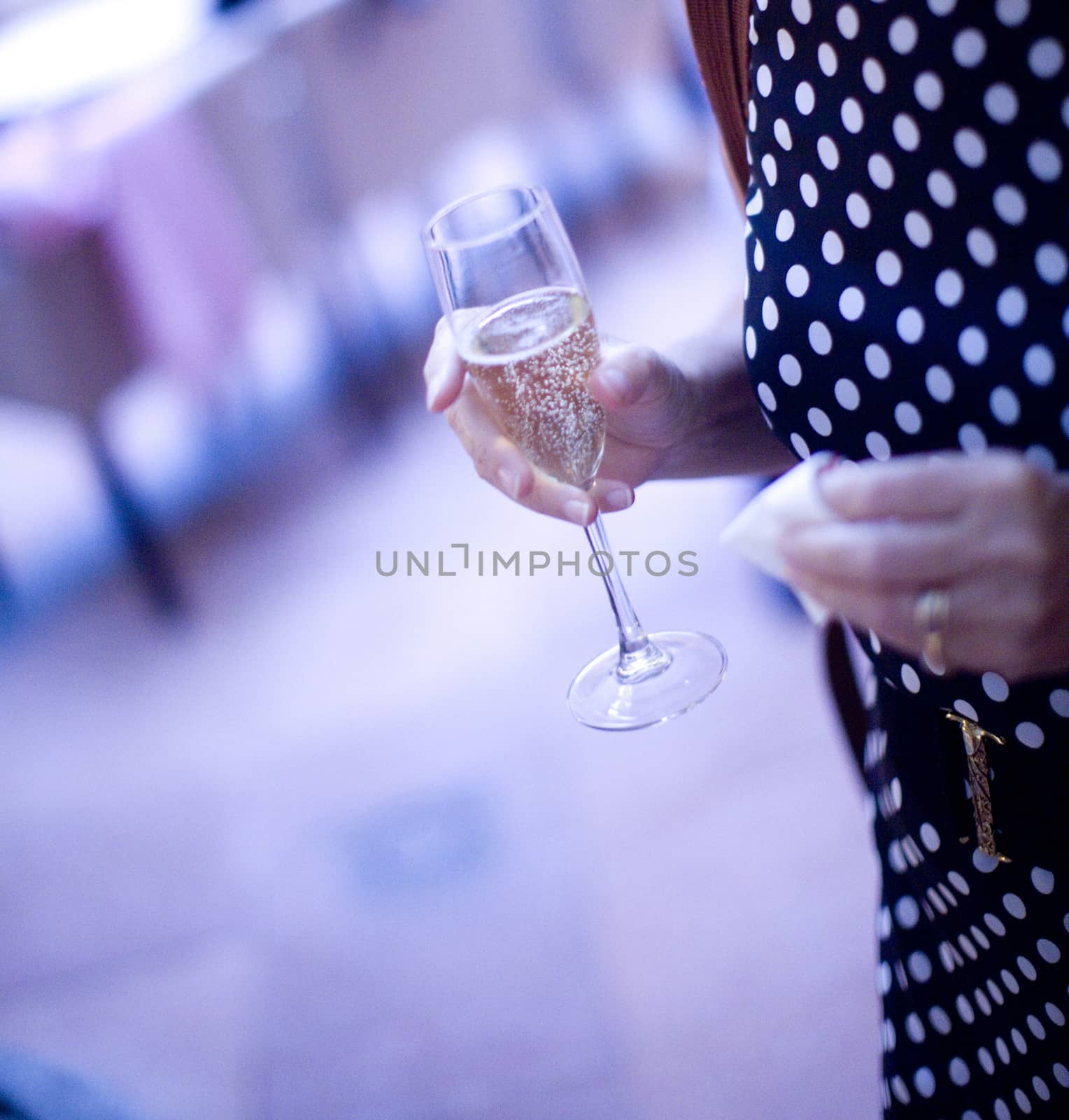 Champagne flute wine glass in hand of young woman female wedding guest with black and white spotty dress.