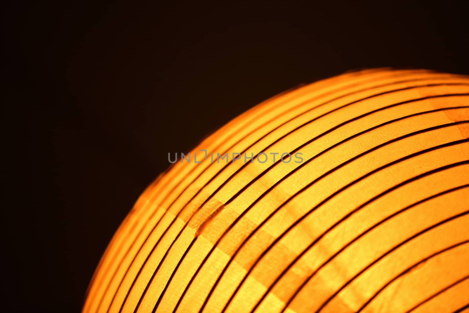Orange yellow Chinese traditional paper lantern light in curved line semi abstract image on plain black studio background. 