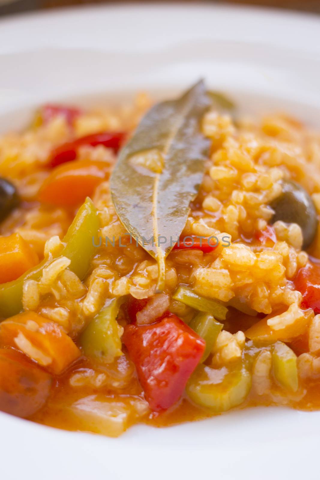 Spanish vegetarian vegetable soup rice dish "Arroz caldoso" like Paella with tomato, red and green peppers, carrot and olives on plate with bay leaf on top. 