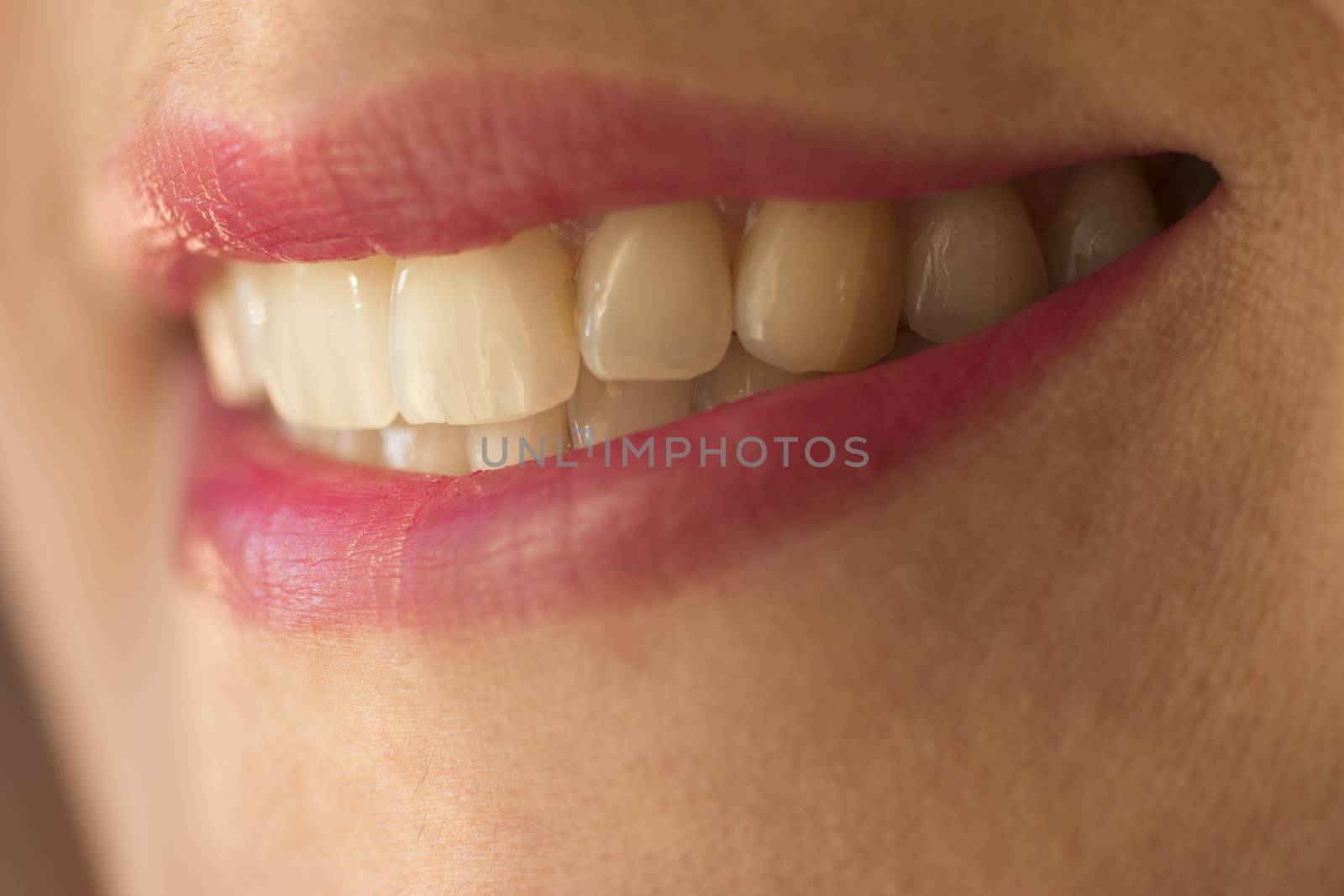 Macro close-up shot of mouth of woman aged 30-35 showing with straight teeth and pink lipstick. 