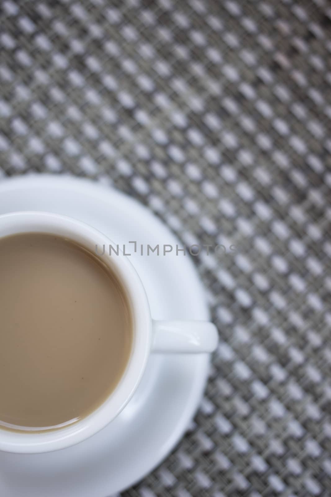 Coffee expresso with milk in cup and saucer shot from above on grey tablecloth patterned background unfocused. 