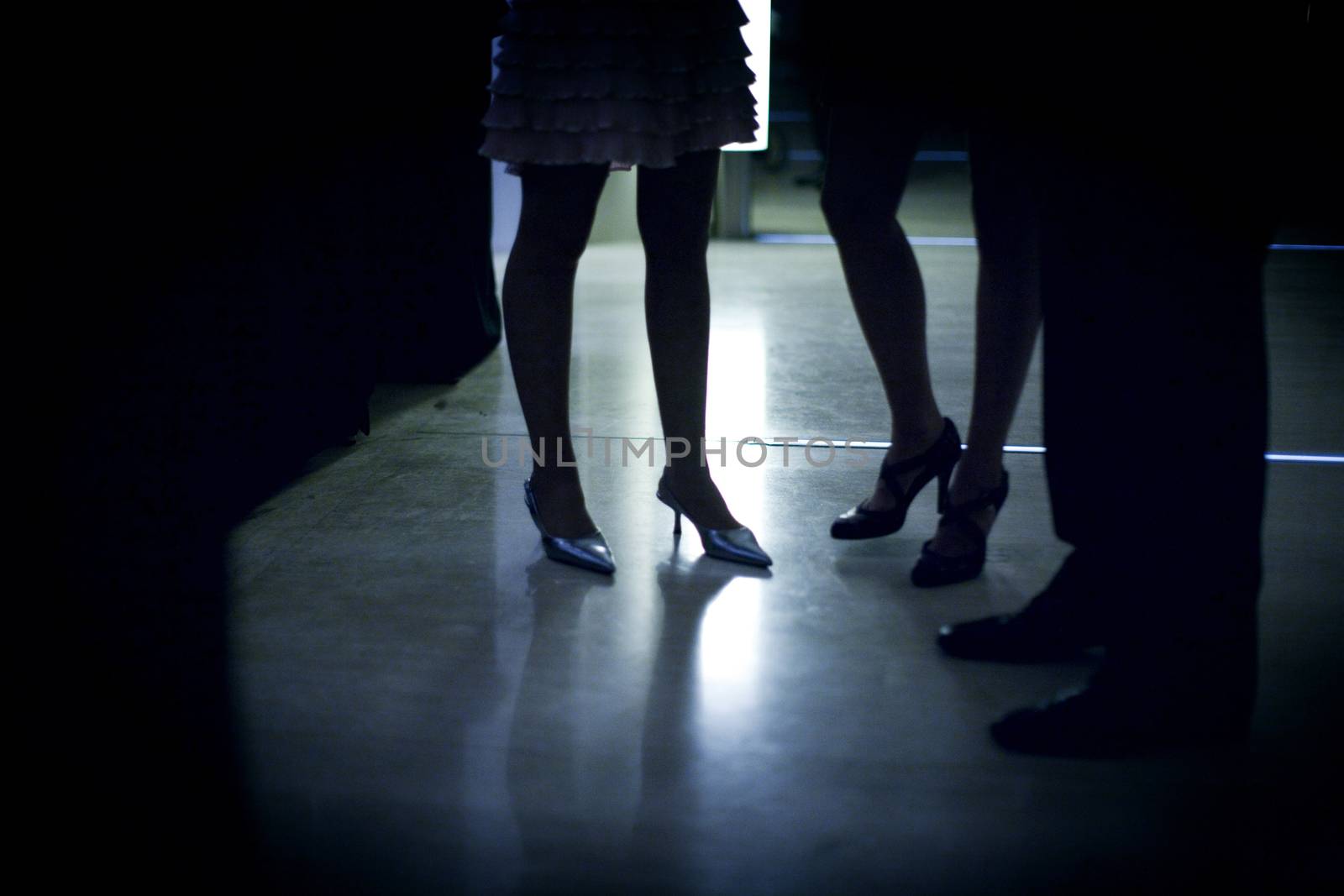 Feet of young woman wedding guest in high heel shoes and cocktail party dress in wedding reception in silhouette.