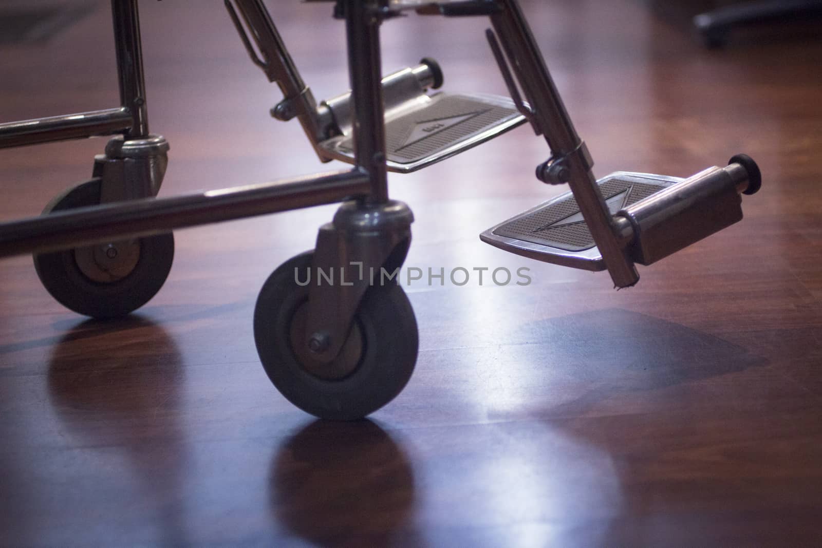 Wheel chair wheels and foots rests in hospital clinic artistic in semi silhouette with waiting room defocused behind. Color digital photo in purple blue tones shot with shallow depth of focus. 