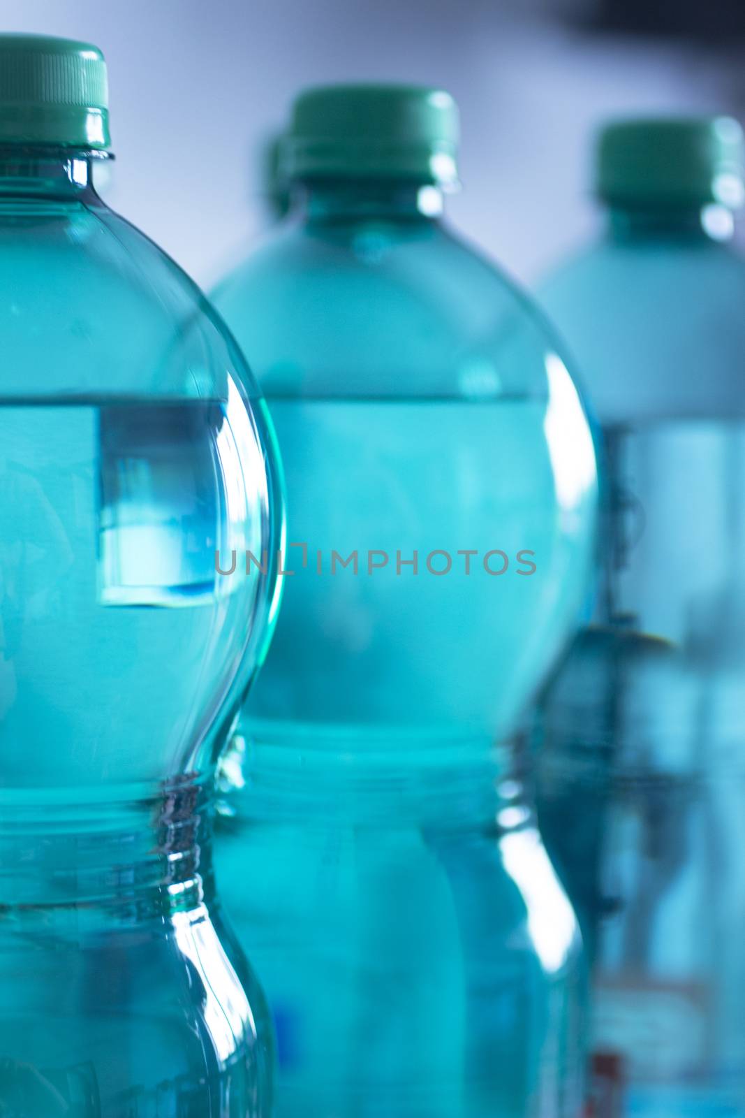 Group of four isolated green plastic water bottles on a plain blue studio background close-up photo.