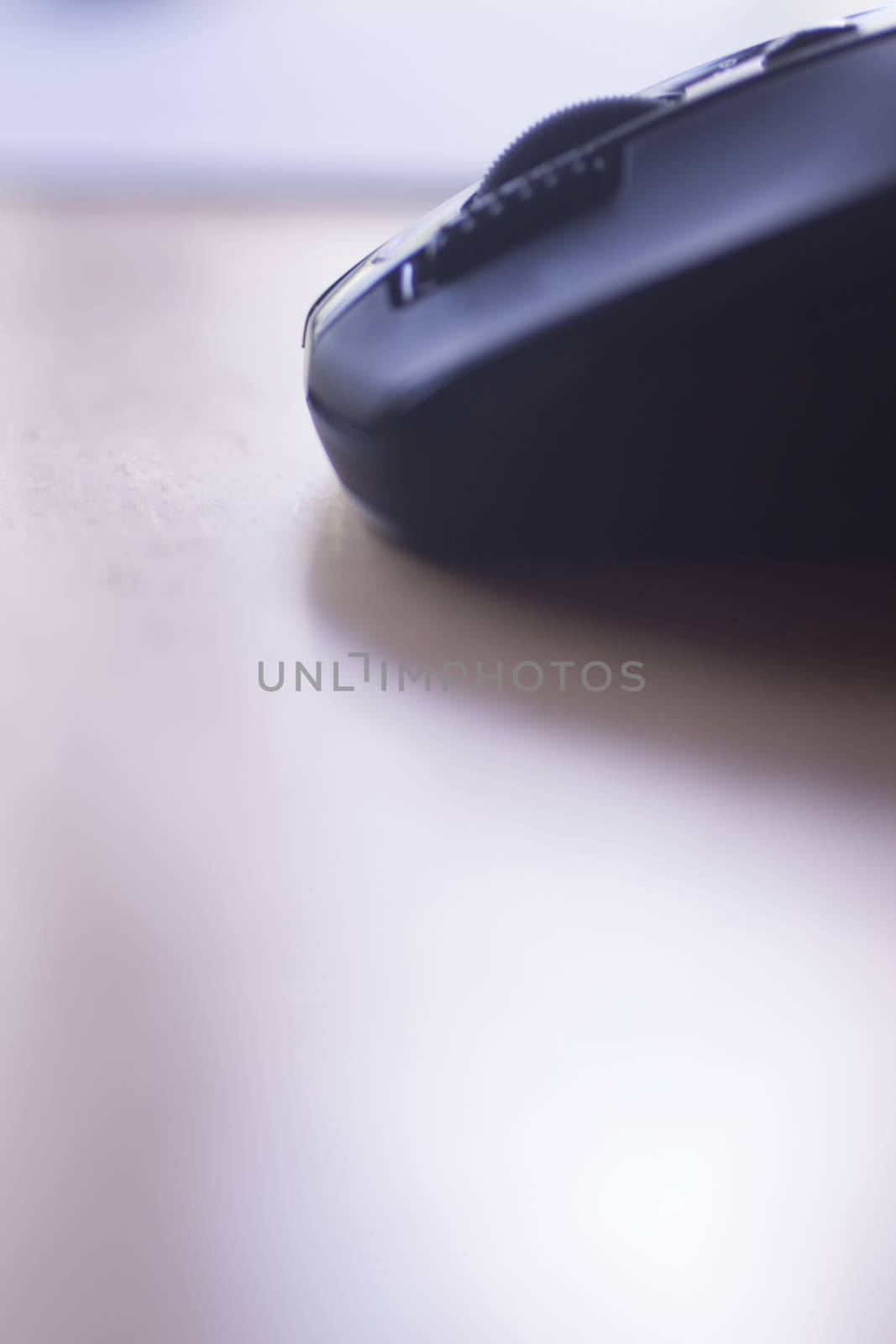 Color photo of a computer pc wifi mouse on work desk office table with shallow depth of focus in blue purple colour. 