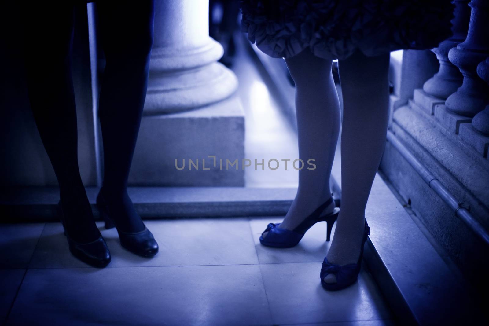 Legs of young ladies wearing high heels shoes and short cocktail dresses standing on shiny tile floor in social event wedding party in Madrid Spain. Blue evening tone color photograph. 