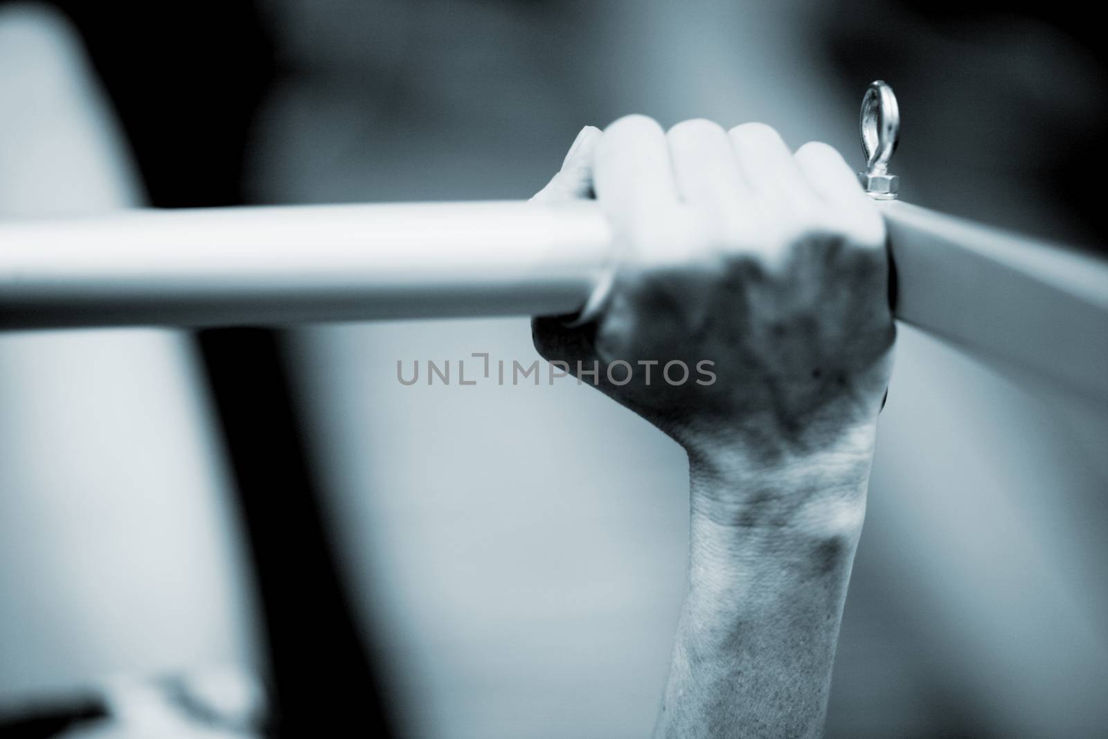 Hand of a young woman realising an exercise of pilates on a pilates machine bar in a healthclub gym specialized training room. Black and white monochrome photo in blue tone. 