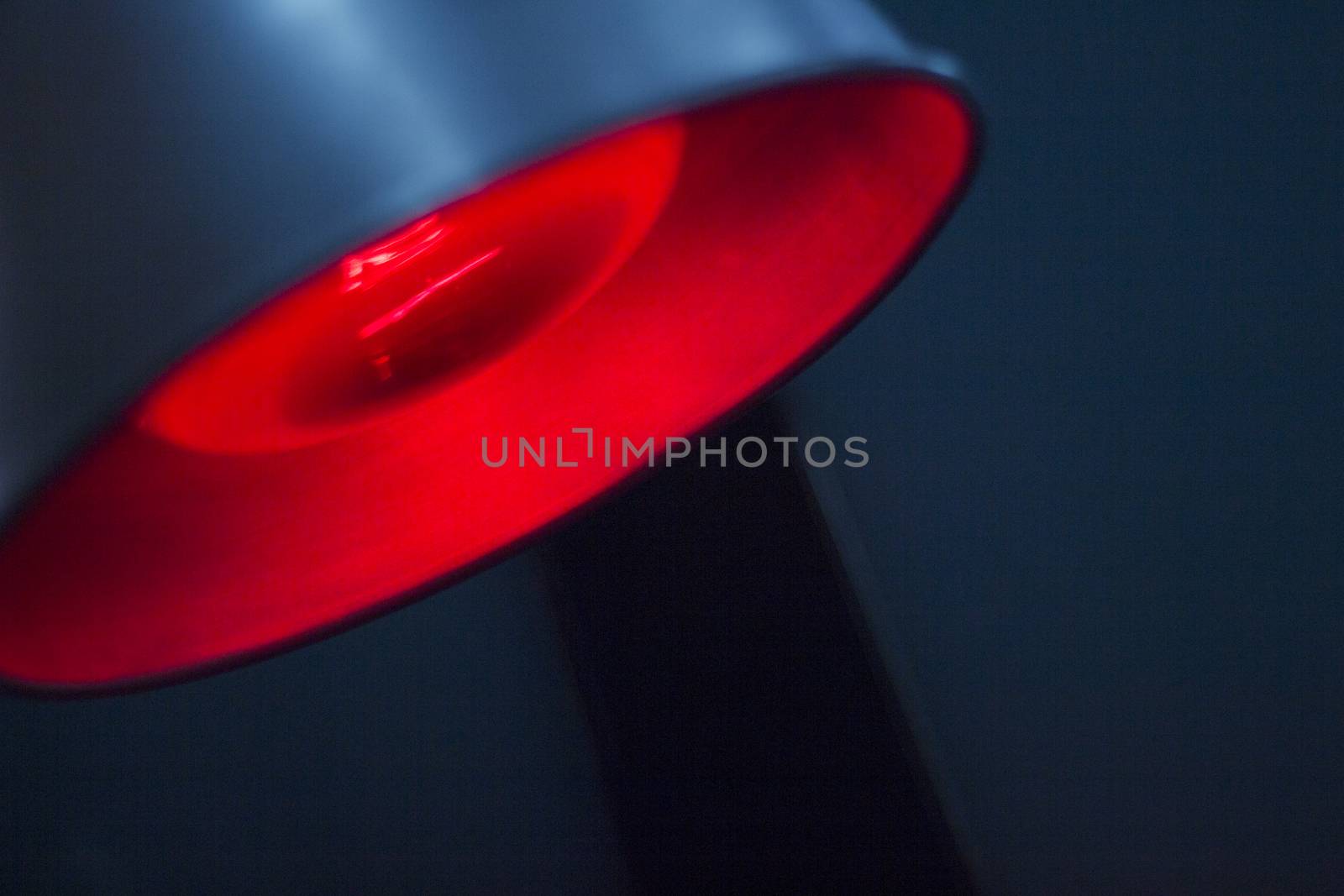 Closeup color digital photo of the bulb of red physiotherapy heat medical rehabilitation lamp in hospital clinic in artistic blue tones. 