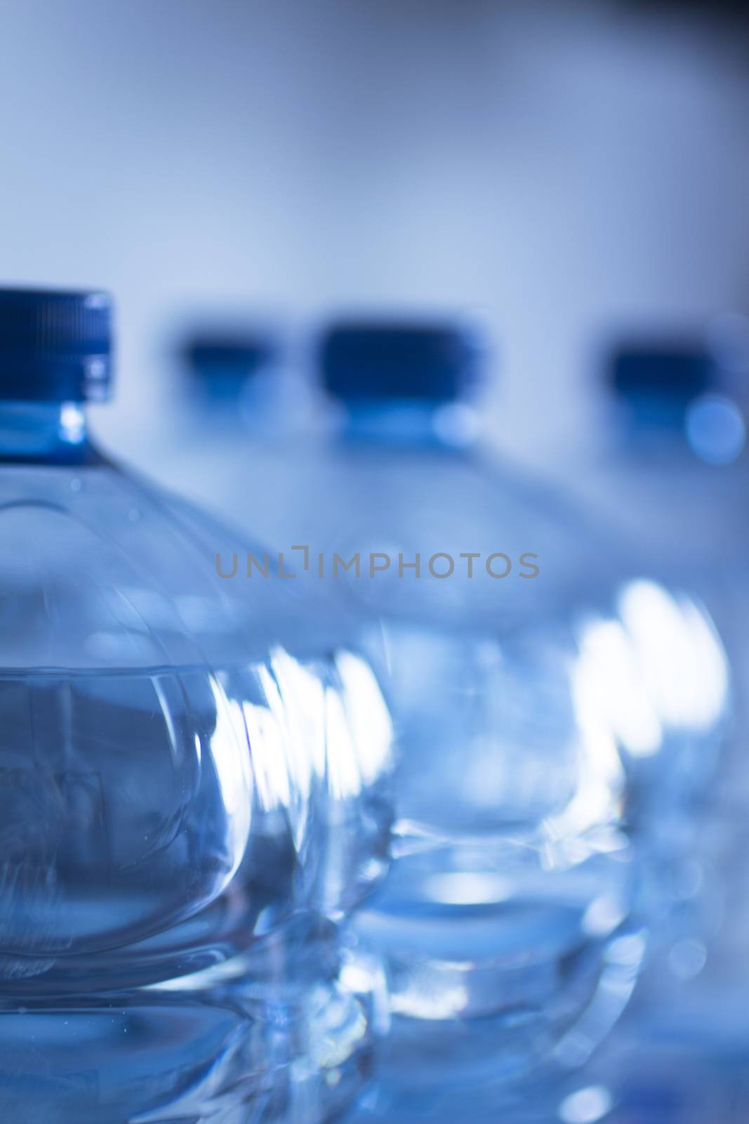 Isolated blue plastic water bottles on a plain blue studio background close-up photo.