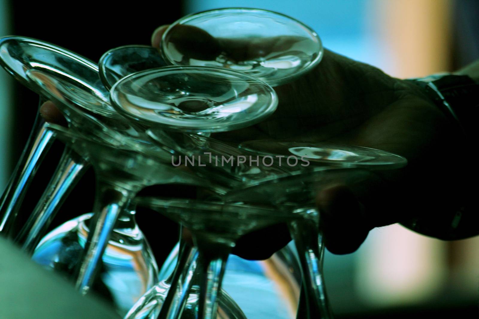 Color photo in blue tones of a group of upturned clear wine glasses sparkling in the light held in the hand of the waiter barman in silhouette in a pub / public house restaurant bar at night in Chueca in Madrid Spain. The multiple glasses have just been washed and dried, and going to be displayed upside-down on the top of the bar ready to be filled with wine and served to the evening's customers. 