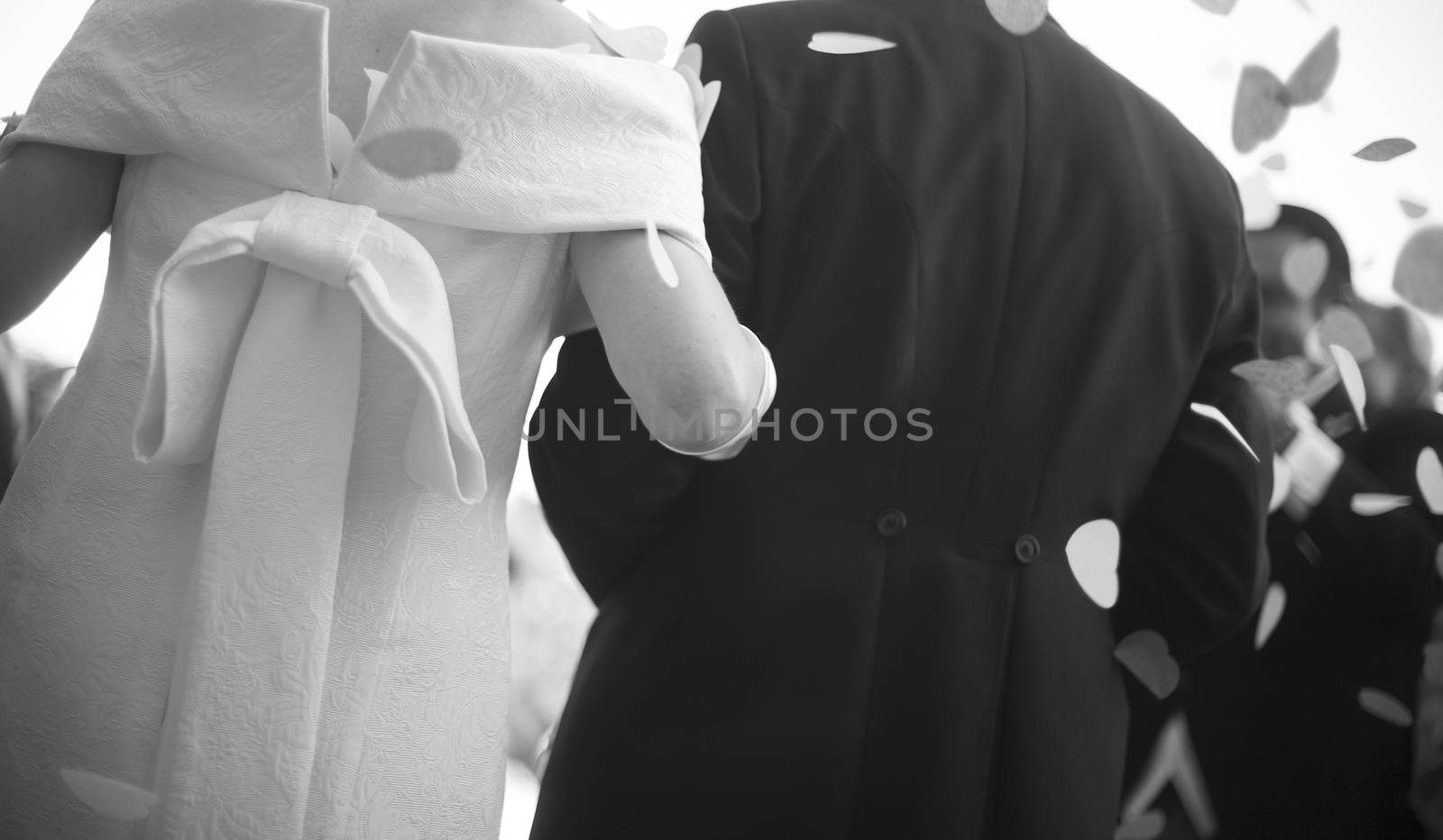 Black and white artistic digital photo of bridegroom in dark suit and white shirt in wedding marriage holding hands with the bride in white long wedding bridal dress. Shallow depth of with background out of focus. 