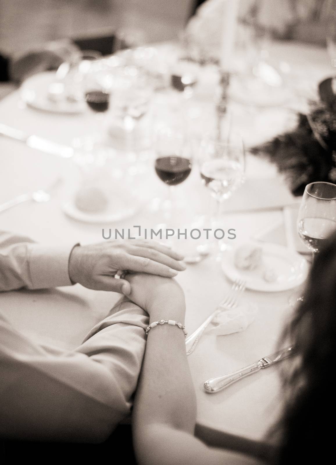 Black and white artistic digital photo of bridegroom in dark suit in wedding marriage event holding hands with the bride in white long wedding bridal dress. Shallow depth of with background out of focus. 