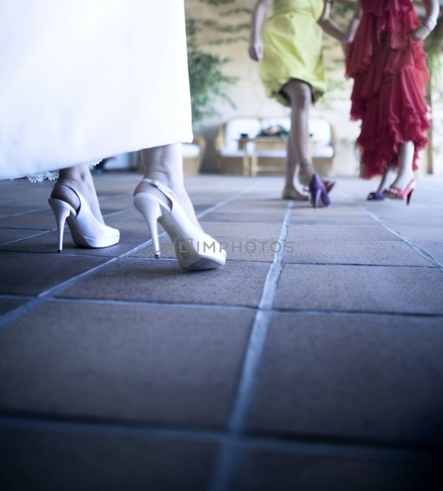 Feet of bride in white high heel shoes and long white wedding dress with female wedding guests defocused. Low angle shot with shallow deth of focus.
