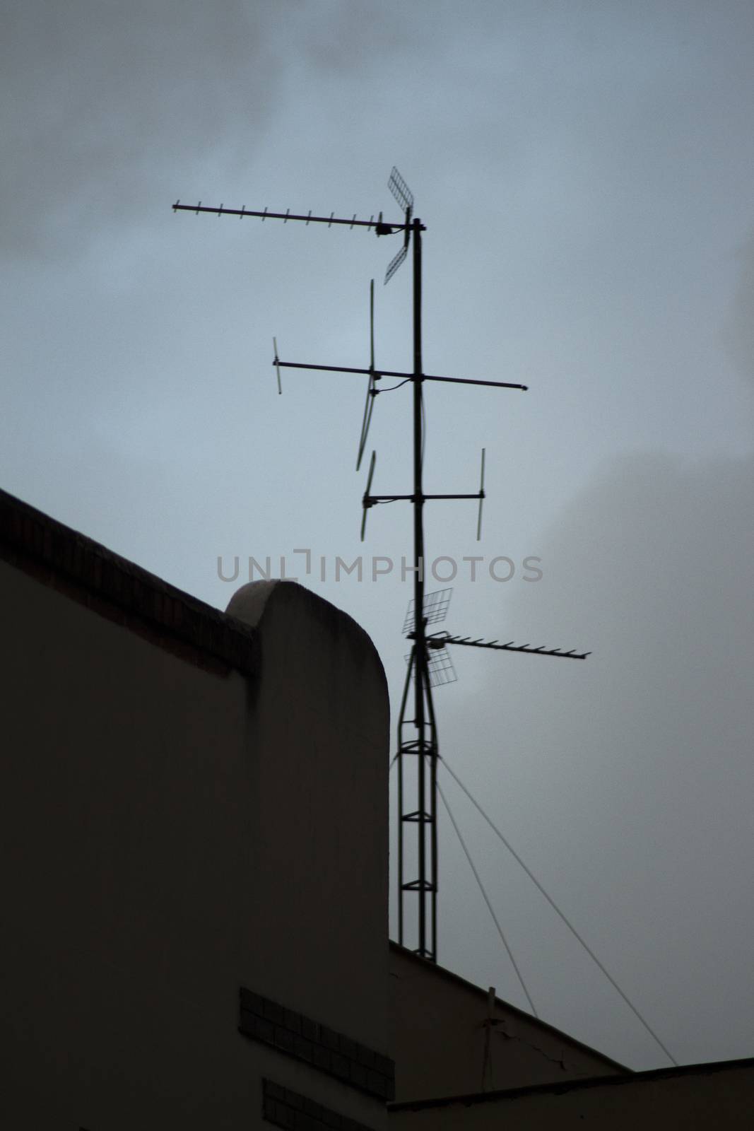 TV arial television antenna tied with metal cables onto roof of a building and blue grey sky in Madrid Spain. 