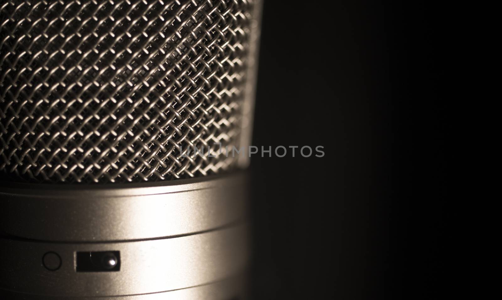 Professional large diaphragm studio voice recording microphone showing metallic body and grill with switch for recording modes. Artistic color digital photo with shallow depth of focus and negative space and white background. 