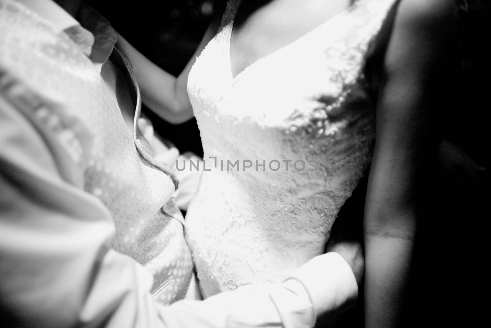 Black and white artistic digital photo of bridegroom in dark suit in wedding marriage event holding hands with the bride in white long wedding bridal dress. Shallow depth of with background out of focus. 