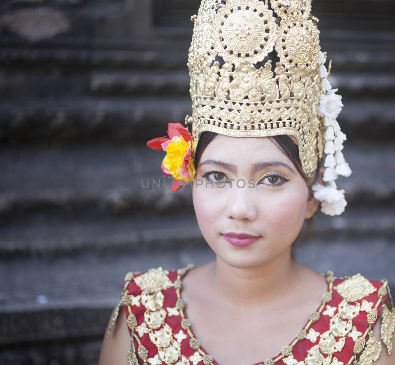 Siem Reap, Cambodia ��� November 27, 2013: Young Cambodian lady dancer in the street wearing traditional Cambodian red and gold dress costume, makeup, ceremonial gold color metal headwear and Cambodian flowers outside Angkor Wat ancient ruined temples looking at the camera before starting traditional dance routine done to earn money from international tourists. Color portrait photo in of a female dancer in the street in Siem Reap Cambodia by Angkor Wat temple ruins in traditional Cambodian dress and headwear with face makeup looking at the camera.

Color portrait photo in of a female dancer in the street in Siem Reap Cambodia by Angkor Wat temple ruins in traditional Cambodian dress and headwear with face makeup looking at the camera. 