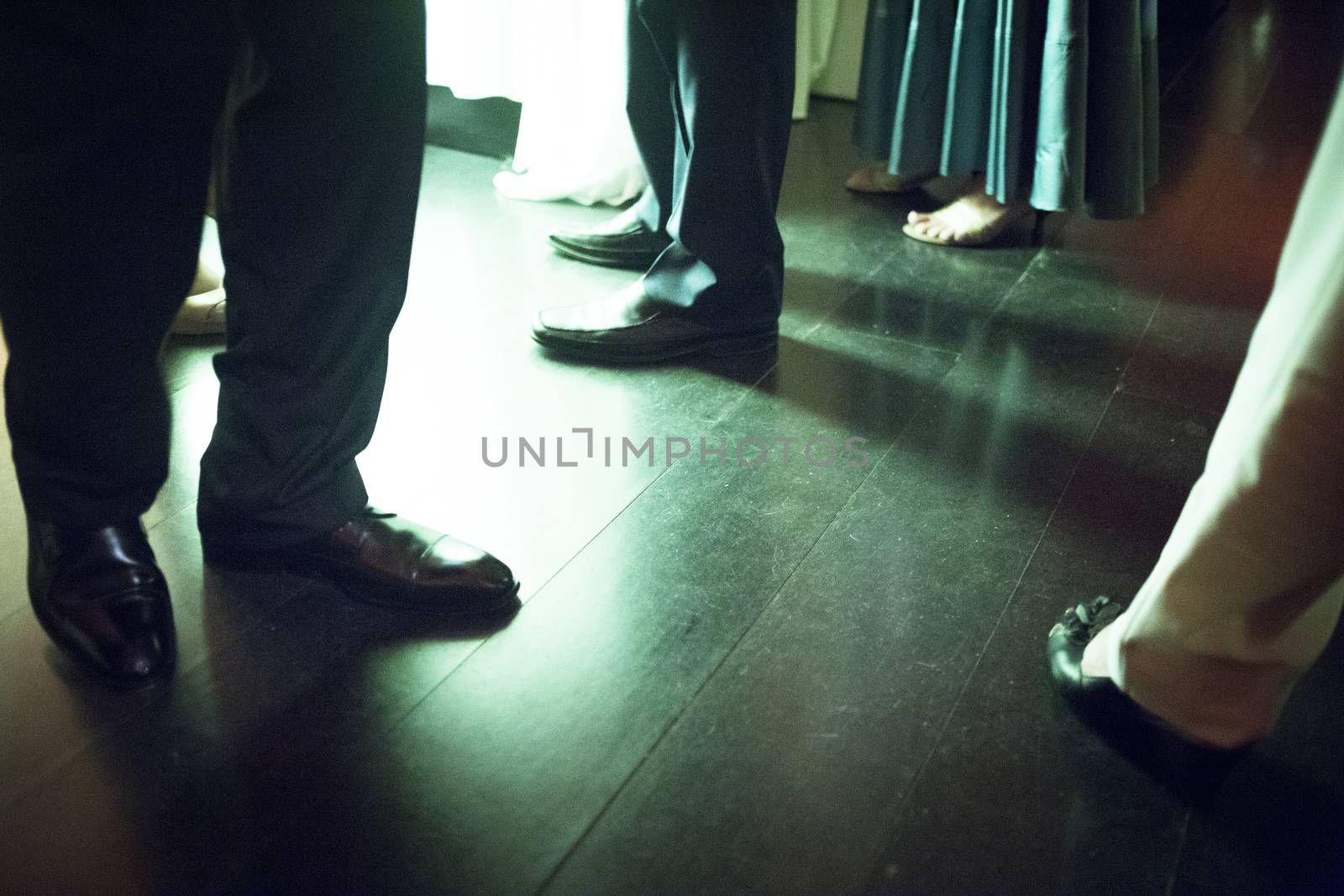 Legs of men and lady wearing standing on shiny tile floor in social event wedding marriage party in Madrid Spain. Green evening night tone color photograph. 