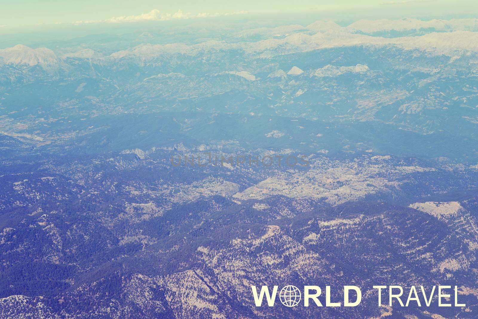 Aerial view of mountainous. wooded. snow-covered terrain. Inscription World Travel and related symbol