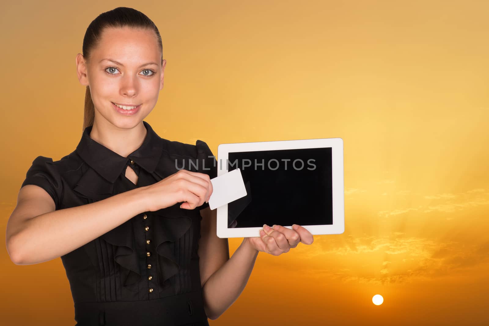 Beautiful businesswoman holding tablet PC and business card in front of screen. Bright sky at sunset as backdrop by cherezoff