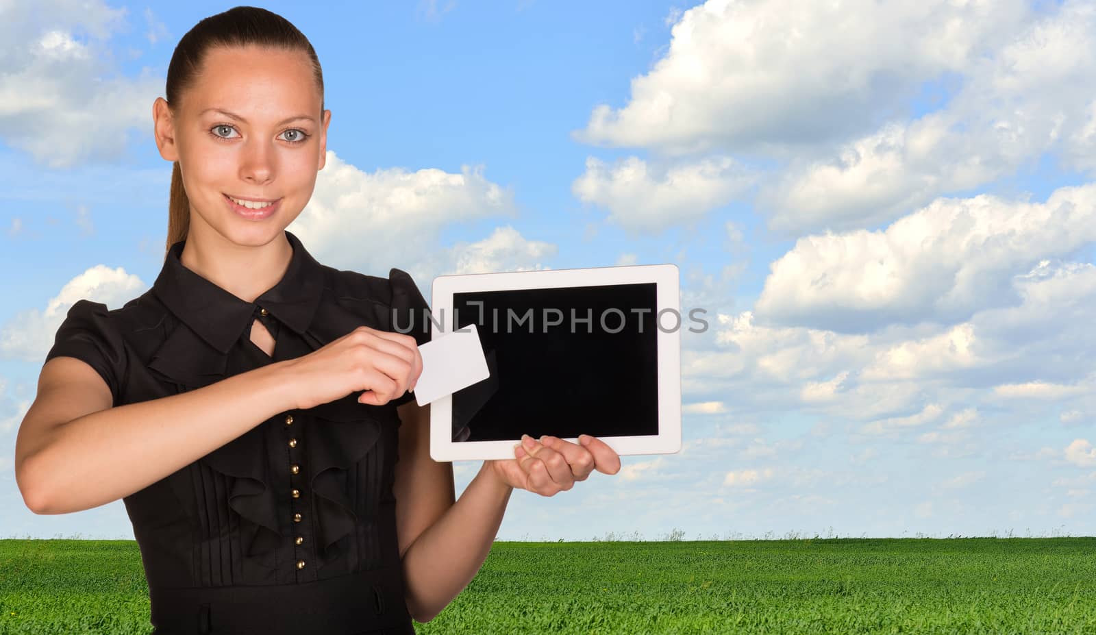 Beautiful businesswoman holding tablet PC. Green meadow, sky and clouds as backdrop by cherezoff