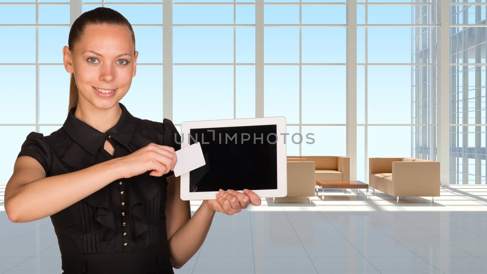Beautiful businesswoman holding blank tablet PC and blank business card in front of PC screen.White roomy hall with sofas and coffee table as backdrop