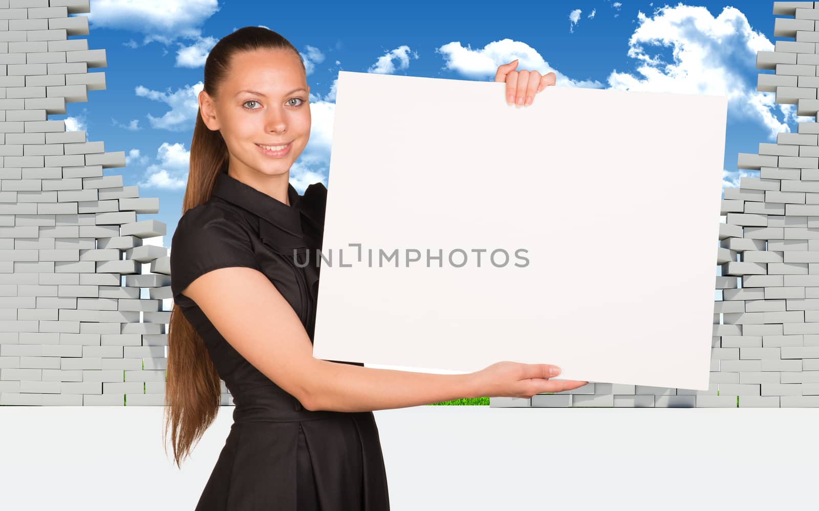 Beautiful businesswoman holding blank paper sheet. Dilapidated brick wall, green meadow and sky as backdrop by cherezoff