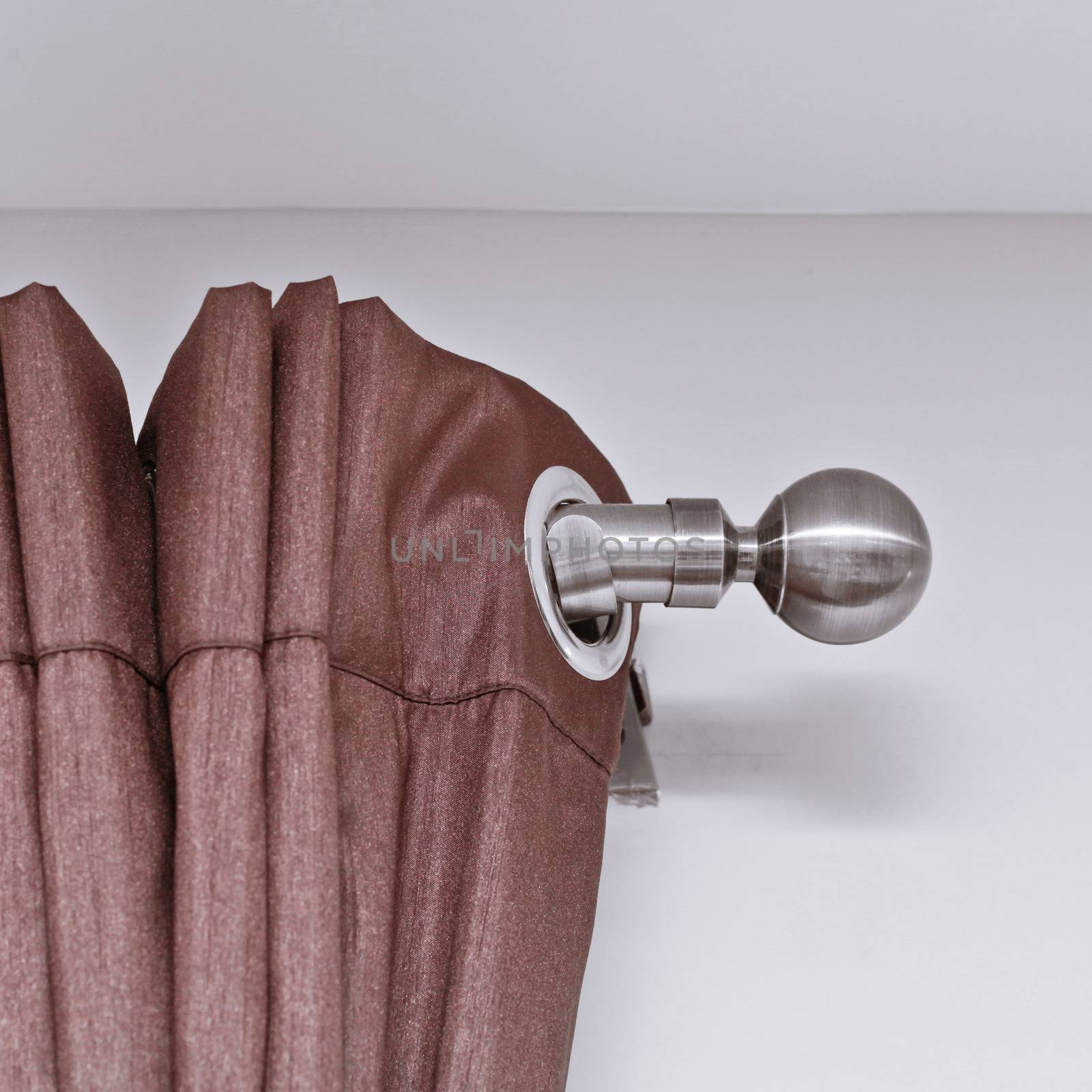 End of a metal curtain pole with a brown curtain