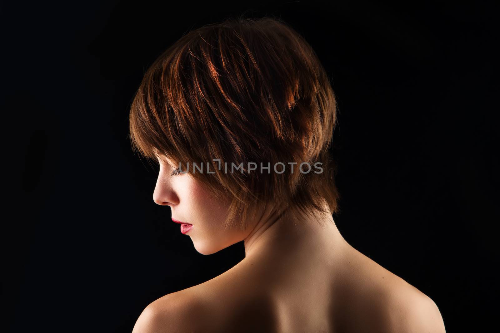 Side portrait of a young woman with short brown hair on a black background