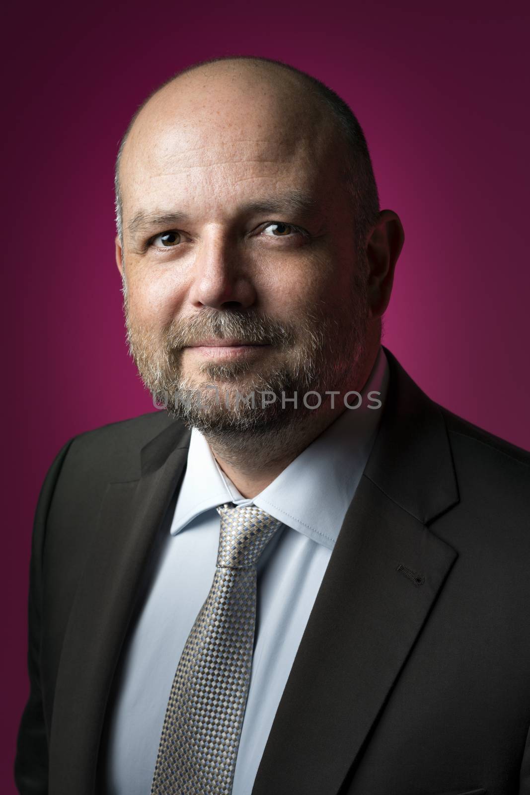 Pleasant businessman in dark suit and tie against magenta background