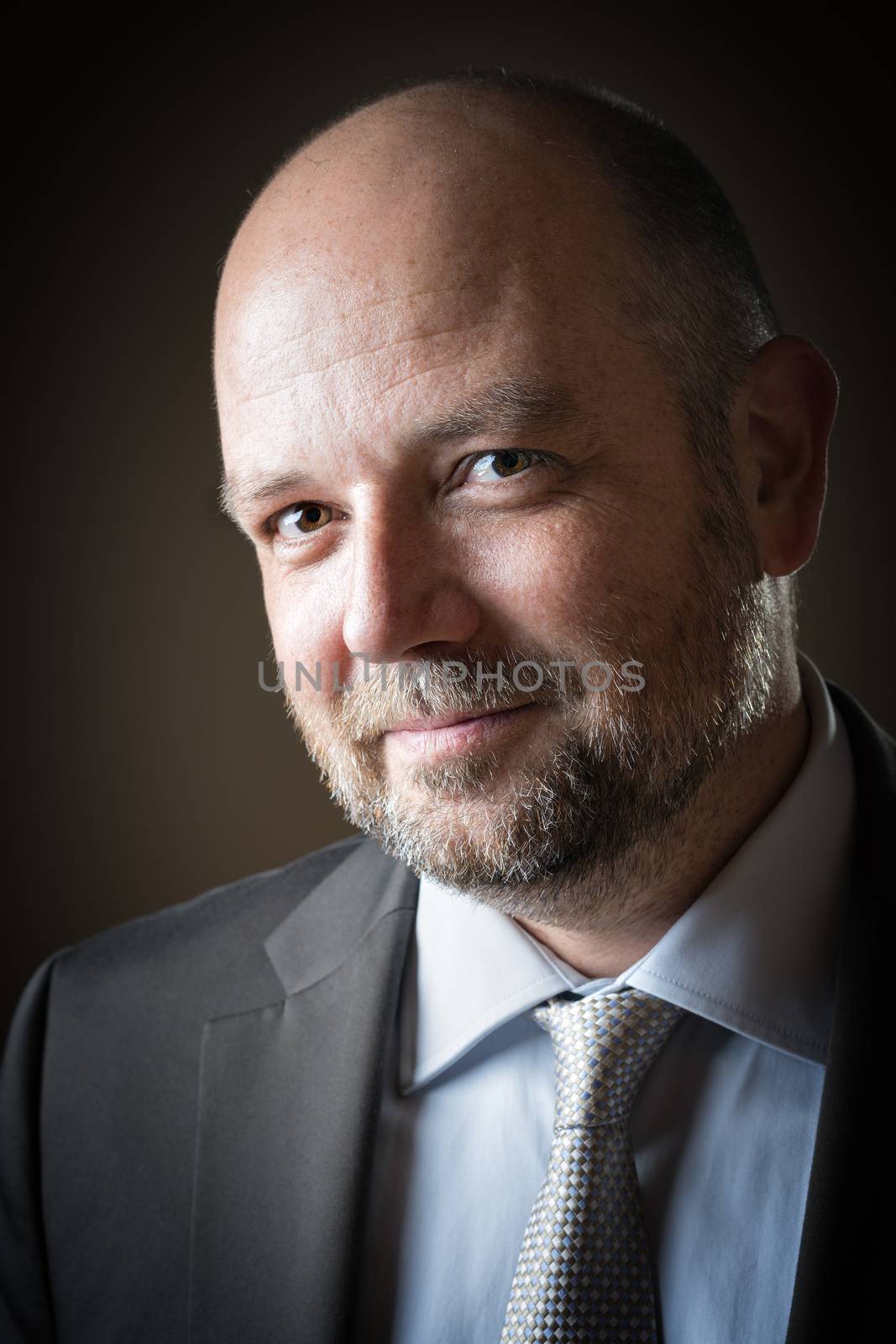 Pleasant business man with beard and bald head against a dark background