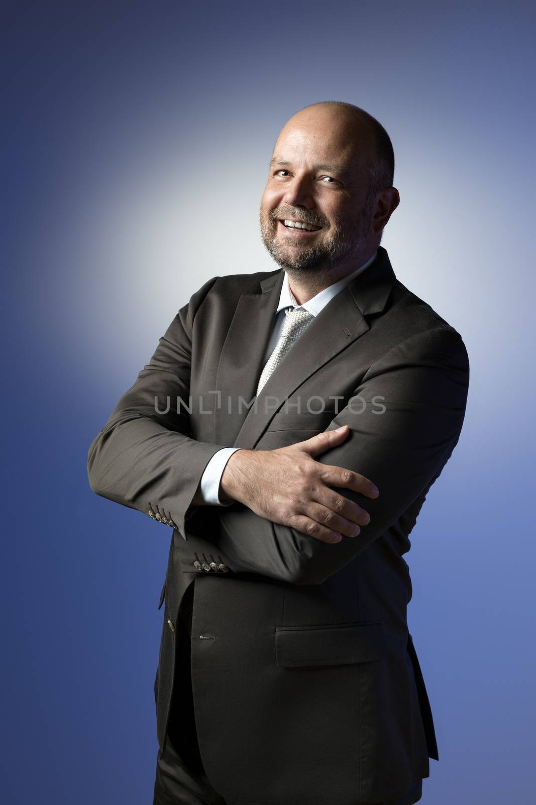 Laughing businessman in dark suit and tie in front of blue background