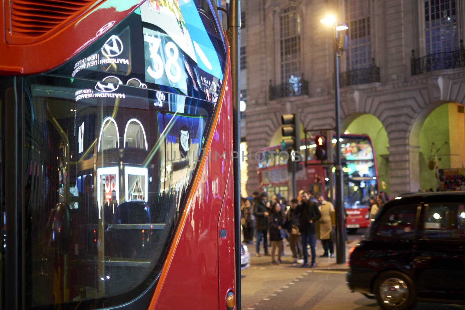 LONDON, UK - DECEMBER 19: Detail of London red bus line 38 reflecting lights of Piccadilly Circus at night, with busy street in the background. December 19, 2014 in London.