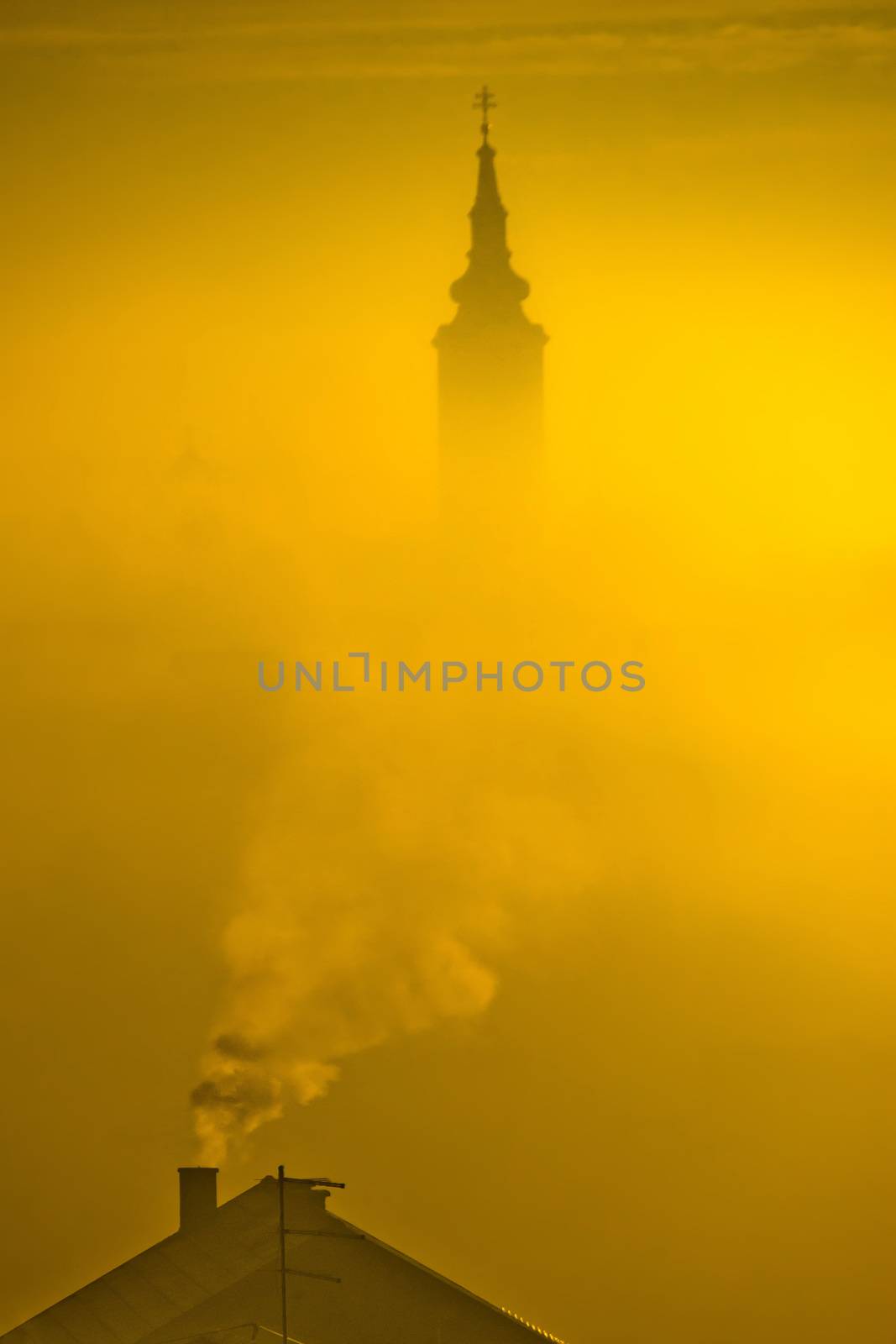 Golden sunrise church tower in fog and chimney smoke in town of Krizevci, Prigorje region, Croatia